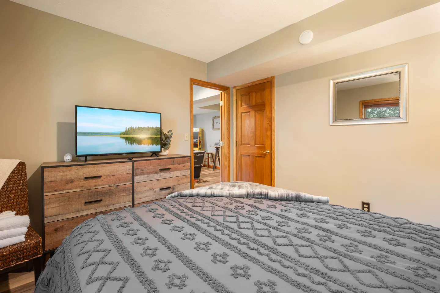 Bedroom featuring a patterned grey bedspread, a wooden dresser with a flat-screen TV, and an open doorway leading to another room.