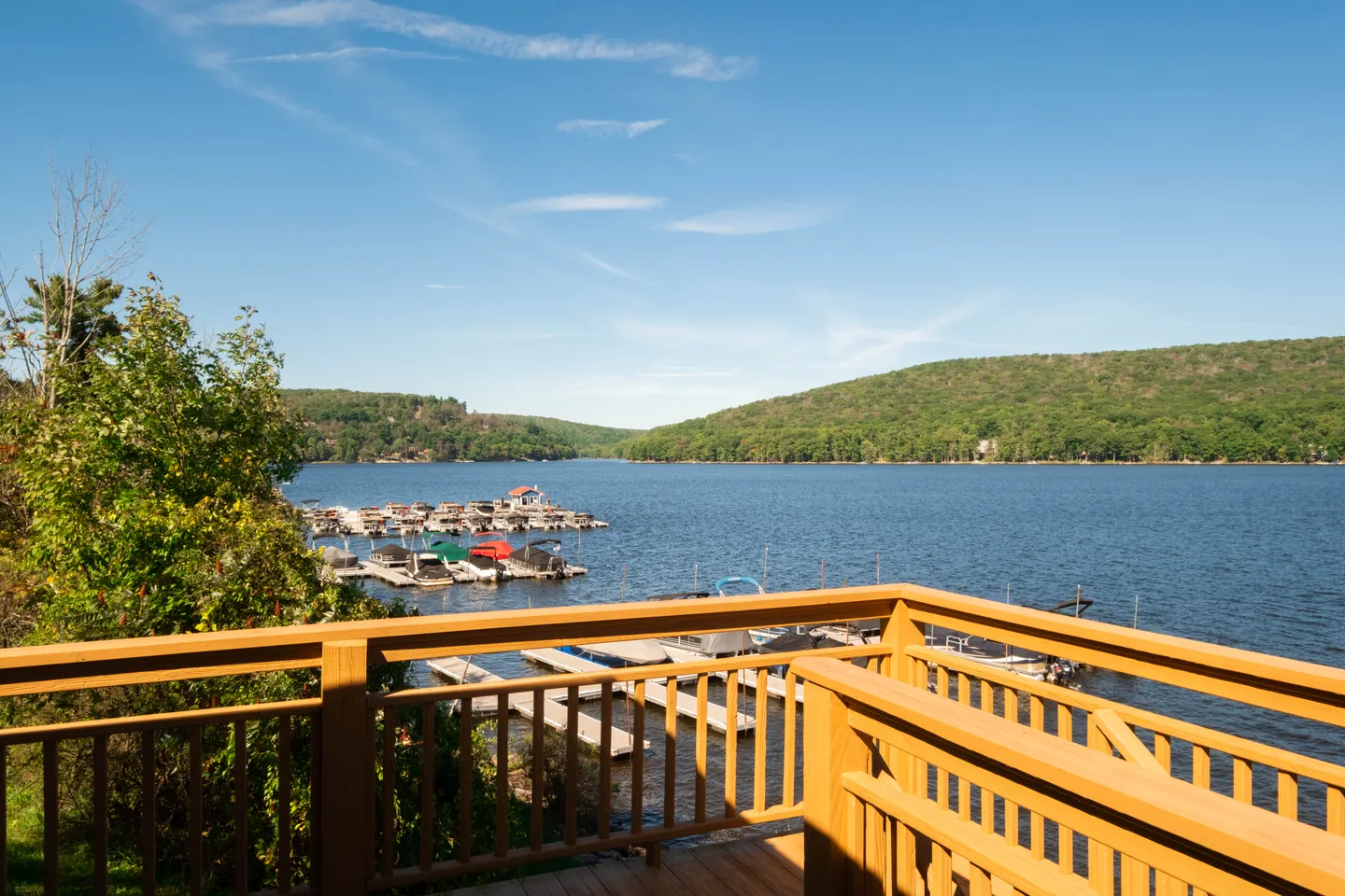 View of a wide lake and boat docks from a wooden deck with railings on a clear, sunny day.