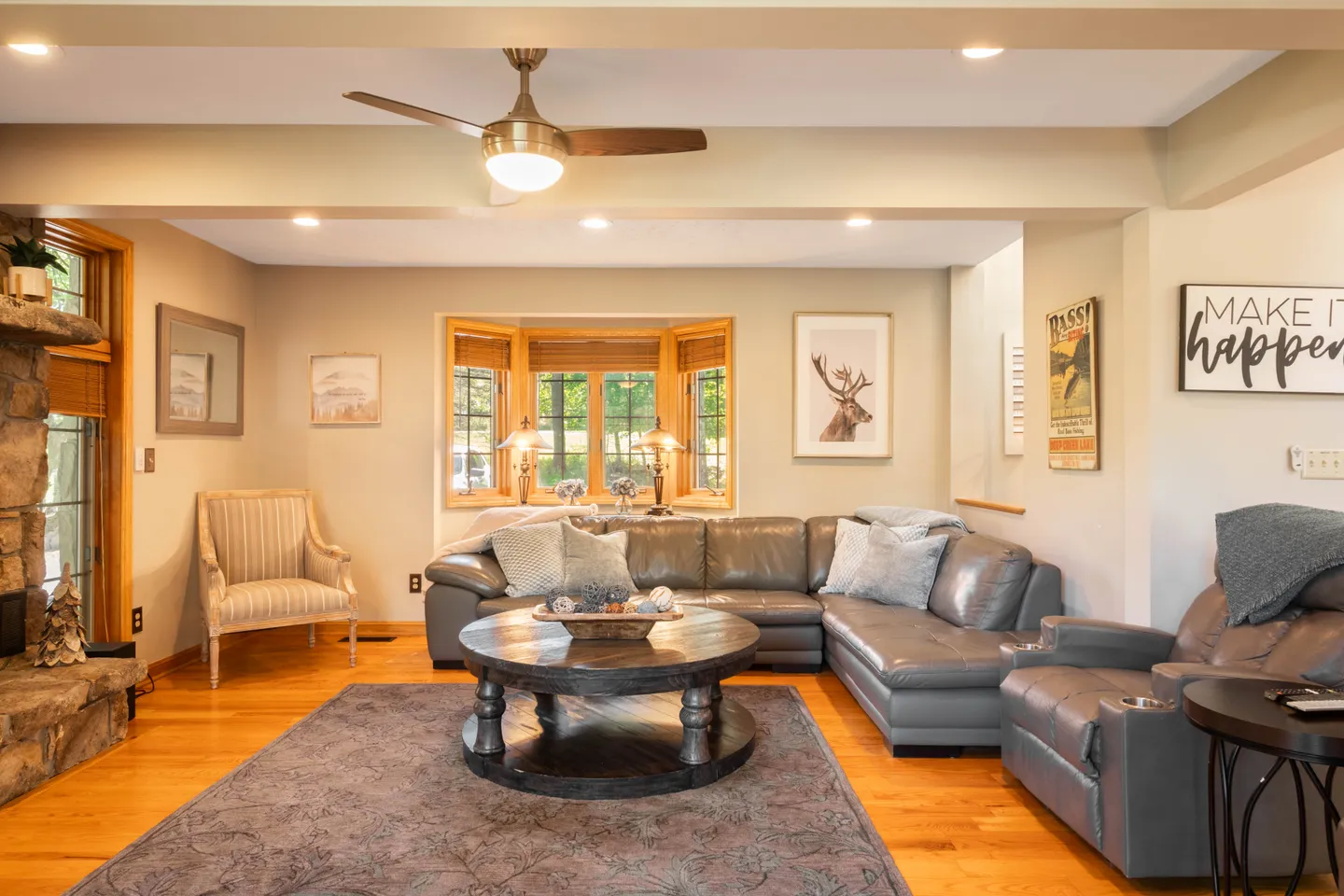 Living room with an L-shaped gray sectional couch, round wood coffee table, stone fireplace hearth, and a bay window in the background.
