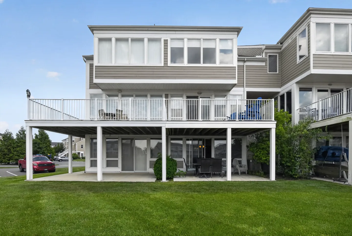Exterior view of the back of a multi-story home featuring a grassy lawn, a ground-floor covered patio with seating, and a second-story open deck with railings.