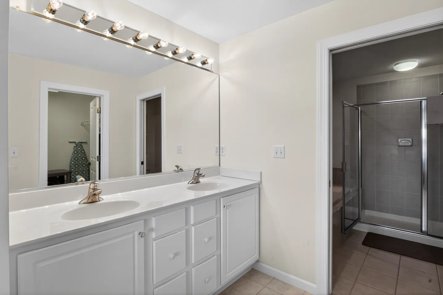 Bathroom with a double sink vanity, large mirror, and an open doorway leading to a tiled walk-in shower.