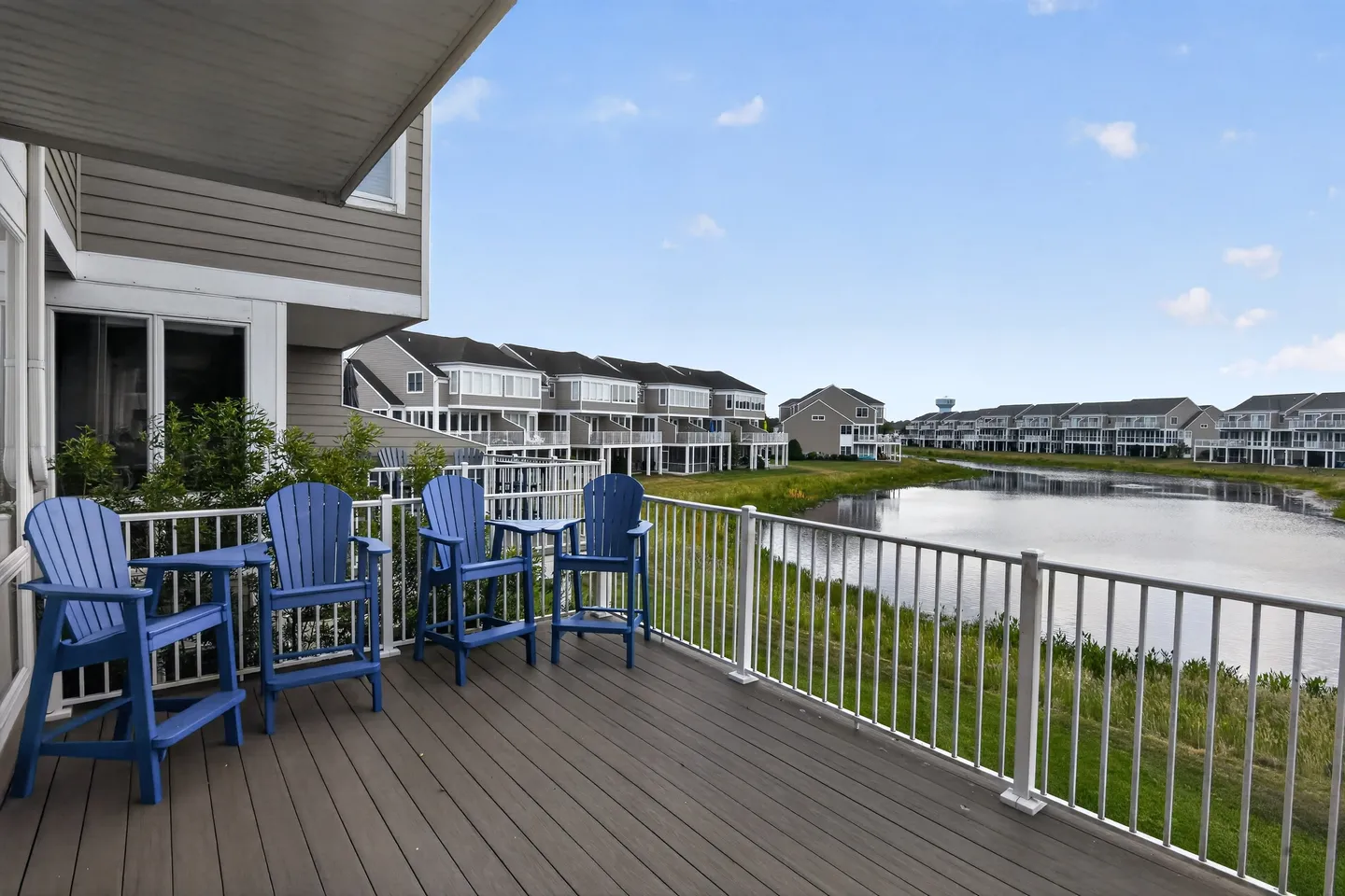 Deck overlooking a pond with blue Adirondack chairs and white railings.