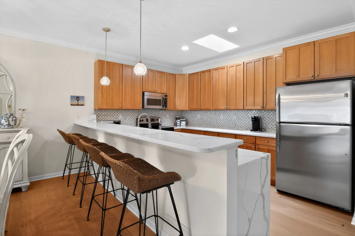 Kitchen with wooden cabinetry, stainless steel appliances, and a breakfast bar with wicker stools.
