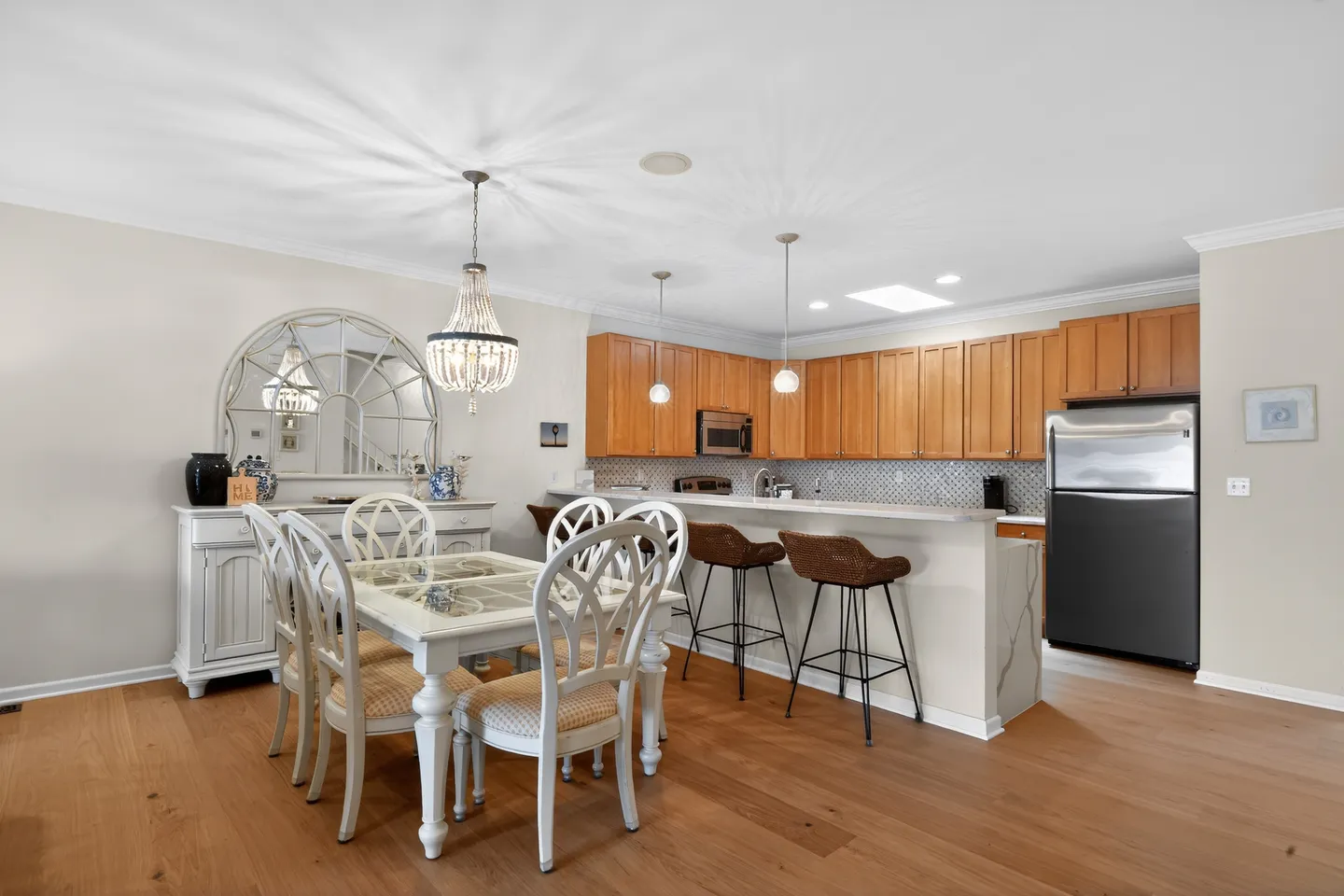 Dining area with a white dining table and chairs adjacent to a kitchen with wooden cabinets and a breakfast bar.