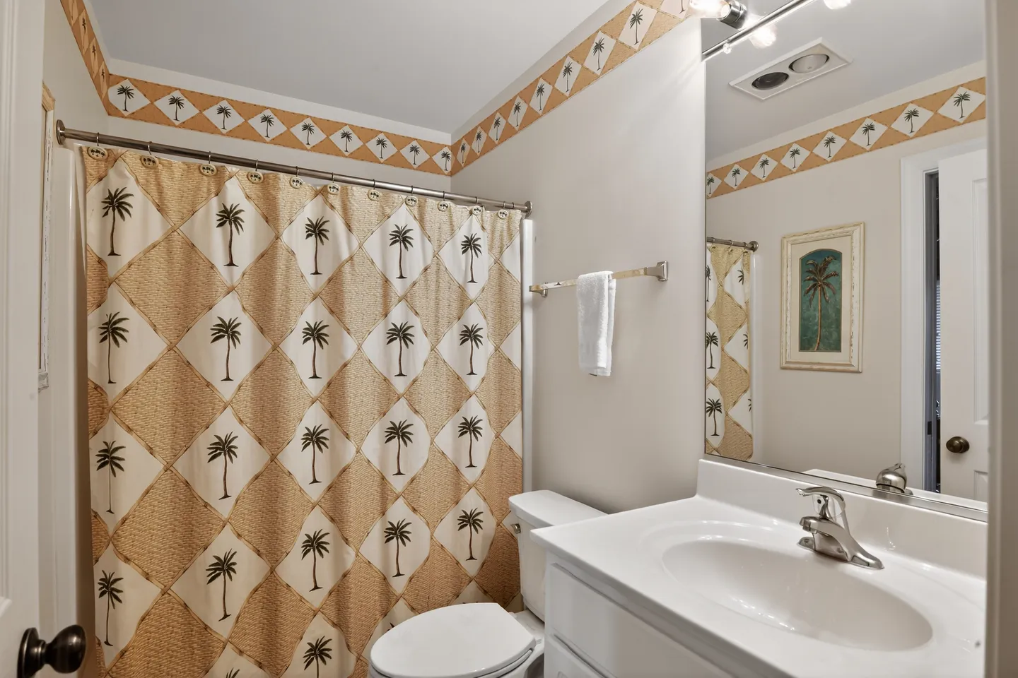 Bathroom showing a vanity sink, toilet, and shower curtain decorated with a palm tree pattern and matching wallpaper border.