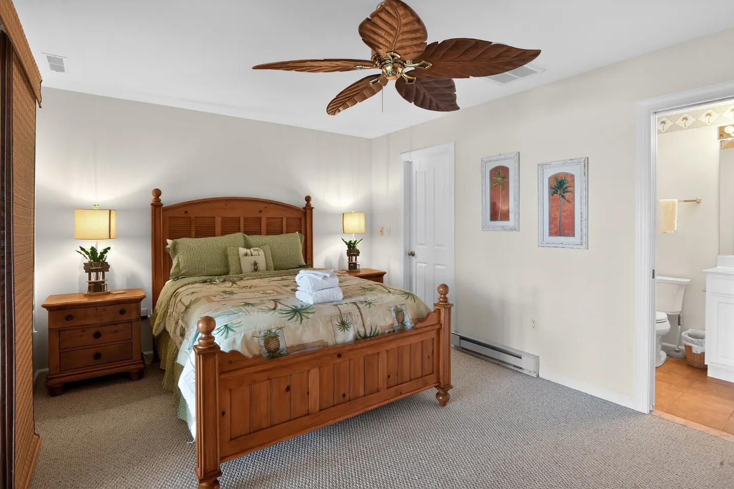 Bedroom with a wooden bed, tropical-style ceiling fan, nightstands with lamps, and an open doorway leading into an en-suite bathroom.