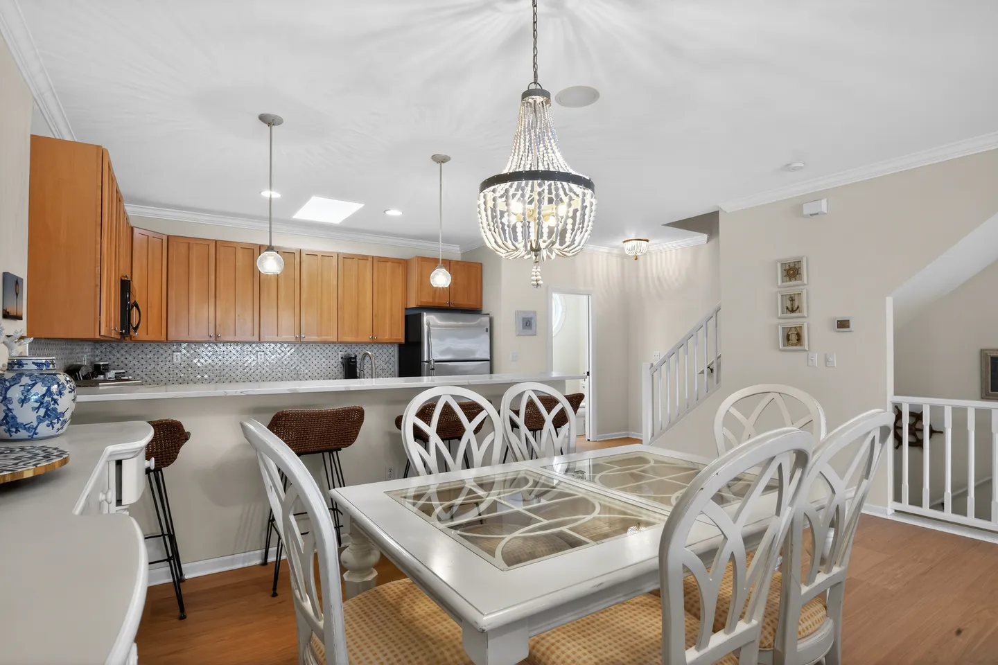 Dining area with a chandelier and white dining table next to an open kitchen with wooden cabinets and a breakfast bar.