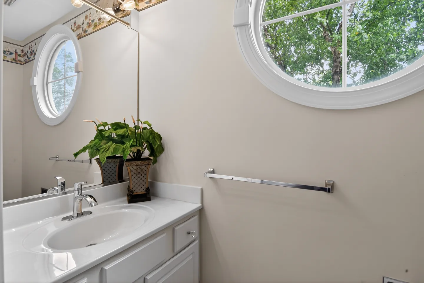 Powder room vanity with white countertop and oval sink beneath a circular window