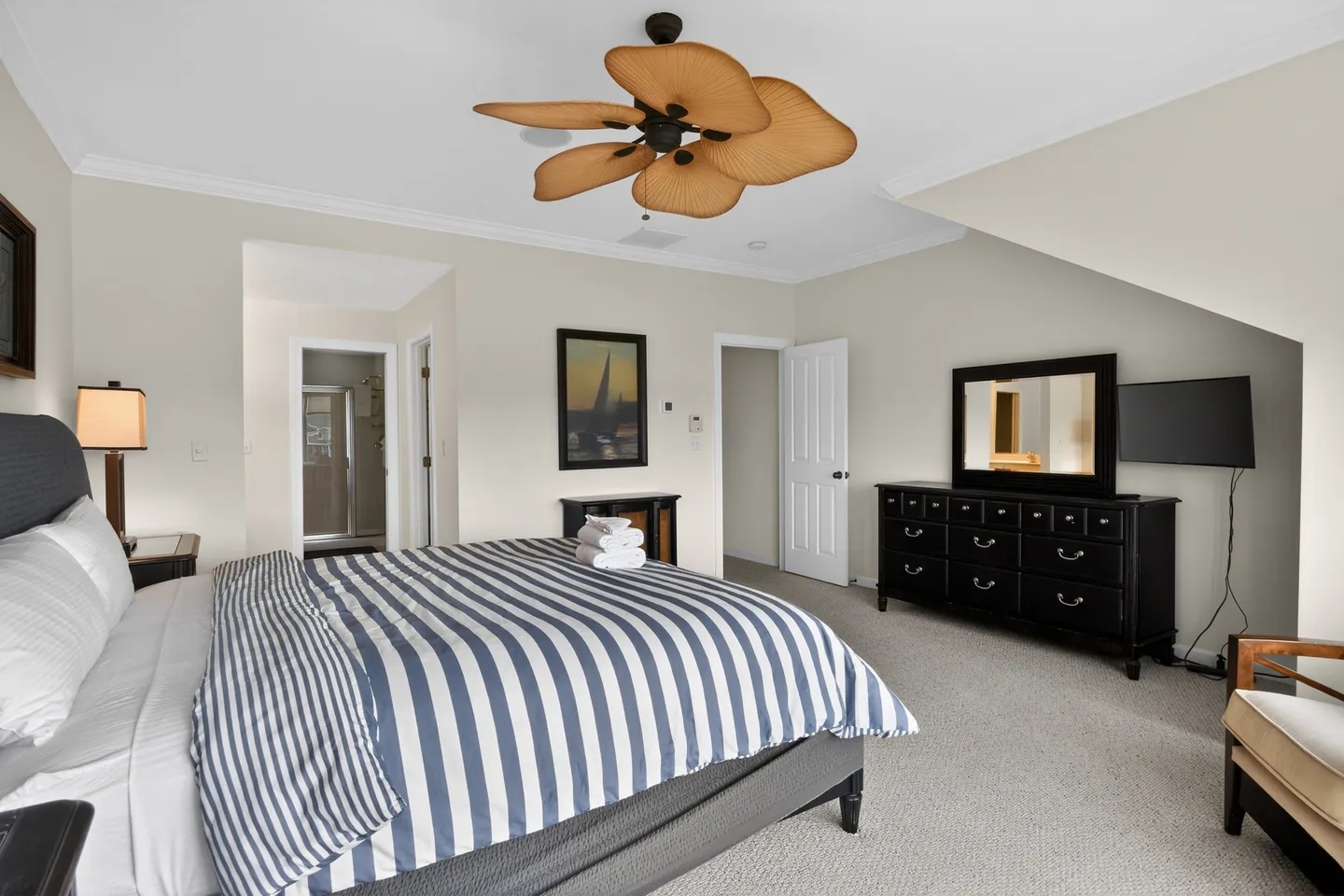 Bedroom featuring a bed with a blue and white striped duvet, a tropical blade ceiling fan, and a black dresser.