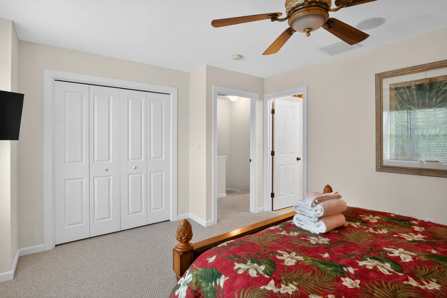 Bedroom with carpeted flooring, a bed featuring a tropical red bedspread, a ceiling fan, and white closet doors.