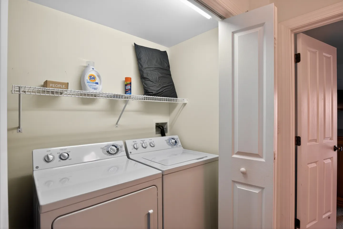 Laundry closet featuring a white side-by-side washing machine and dryer beneath a wire shelf.