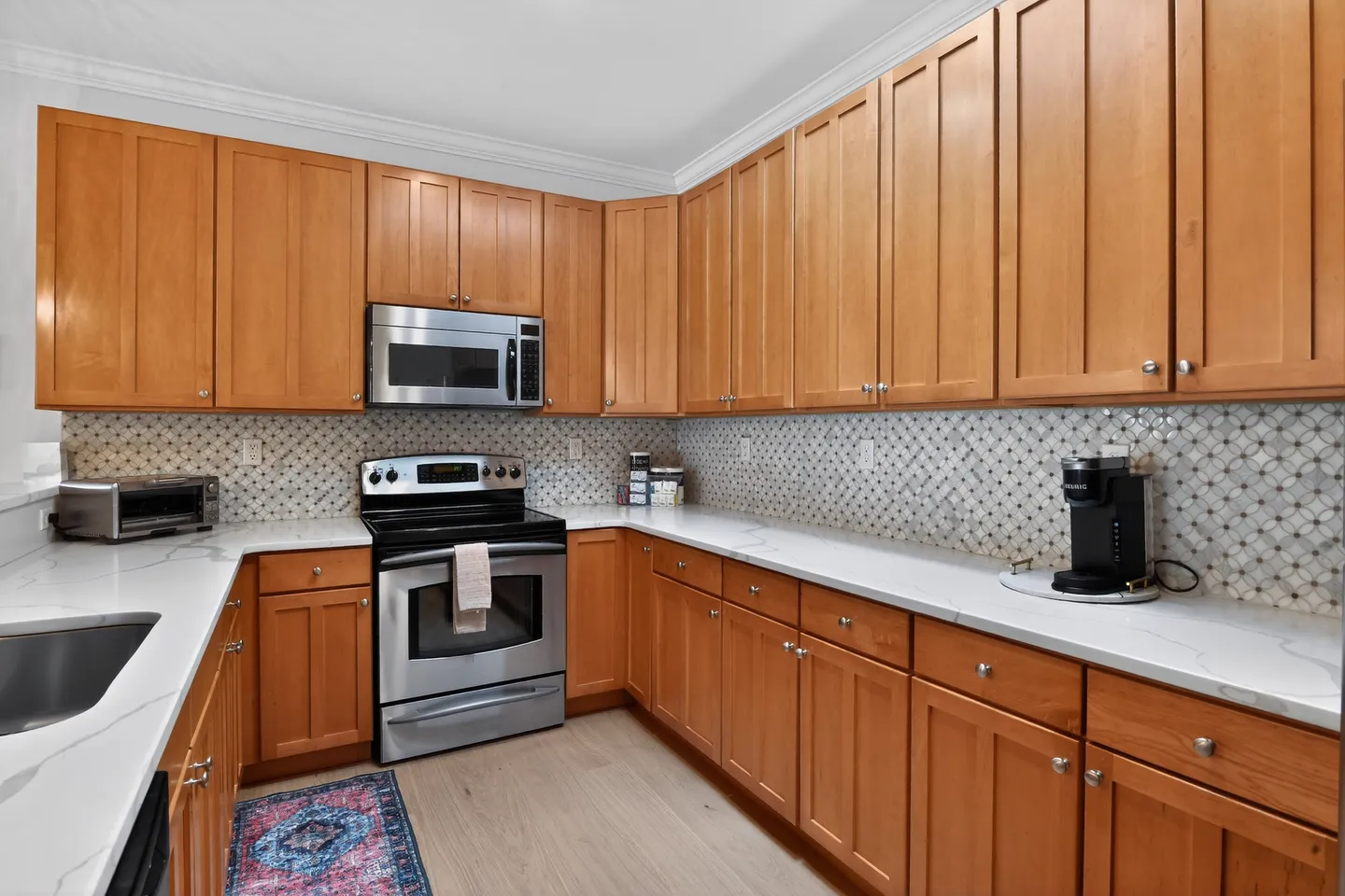 Kitchen with light wood cabinetry, light quartz countertops, patterned tile backsplash, and stainless steel appliances.